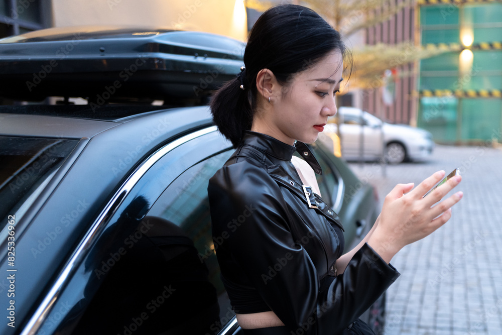 Stylish Asian woman using mobile phone next to car Stylish Asian woman using mobile phone next to car