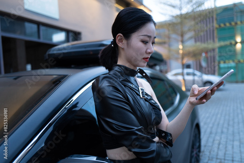 Stylish Asian woman using mobile phone next to car photo