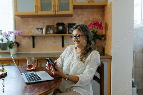 Adult woman using laptop and smartphone at home photo