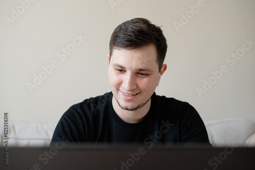 A young smiling man using laptop and wireless headphones photo