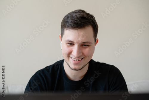 A young smiling man using laptop and wireless headphones photo