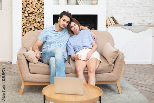 Young married couple sitting on couch and watching movie on laptop. Leisure time and resting concept 