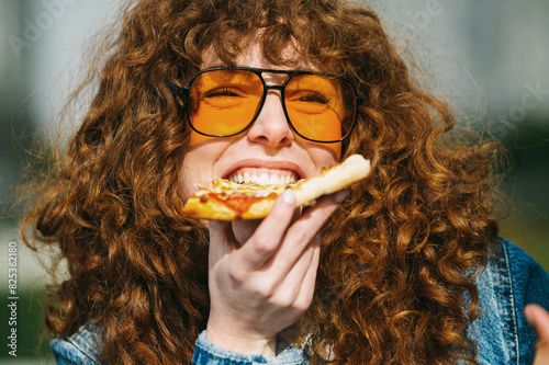 Young woman savoring tasty pizza slice in sunlight photo