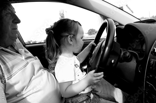 Grandfather teaches little granddaughter to drive a car photo