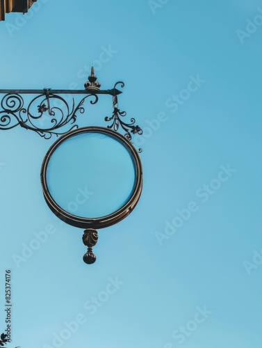 A photo of a round shop sign mockup hanging from an ornate metal bracket, set against a clear sky.