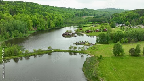 A picturesque aerial shot of a resort area near a lake with cabins, green lawns, and surrounding forested hills. photo