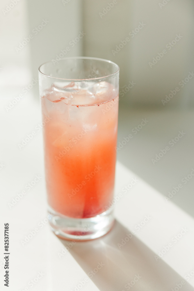 High glass filled with orange juice and an ice cube High glass filled with orange juice and an ice cube