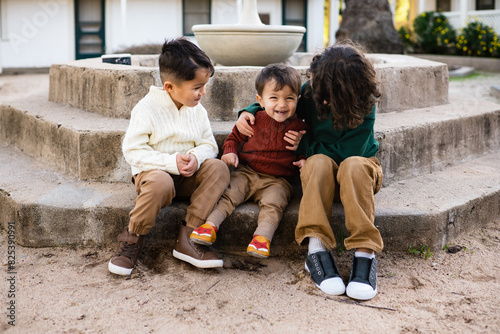 Three young dark haired brothers sit on the steps of a fountain in front of a California adobe in the fall
 photo