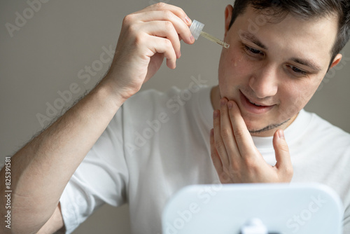 Young man applying cosmetics to his face with a pipette photo