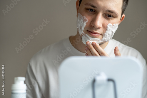 Man applying cleaning or shaving foam on his face in front of mirror photo