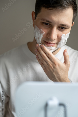 Man applying cleaning or shaving foam on his face in front of mirror photo