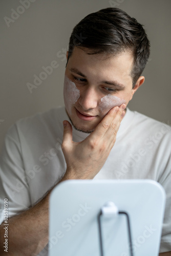 Man applying cream on his face in front of mirror at home environment photo