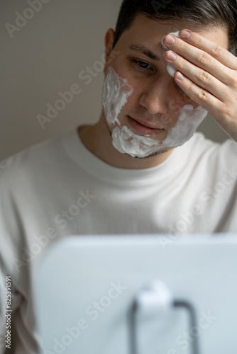 Young man putting cosmetics on his face in front of mirror photo