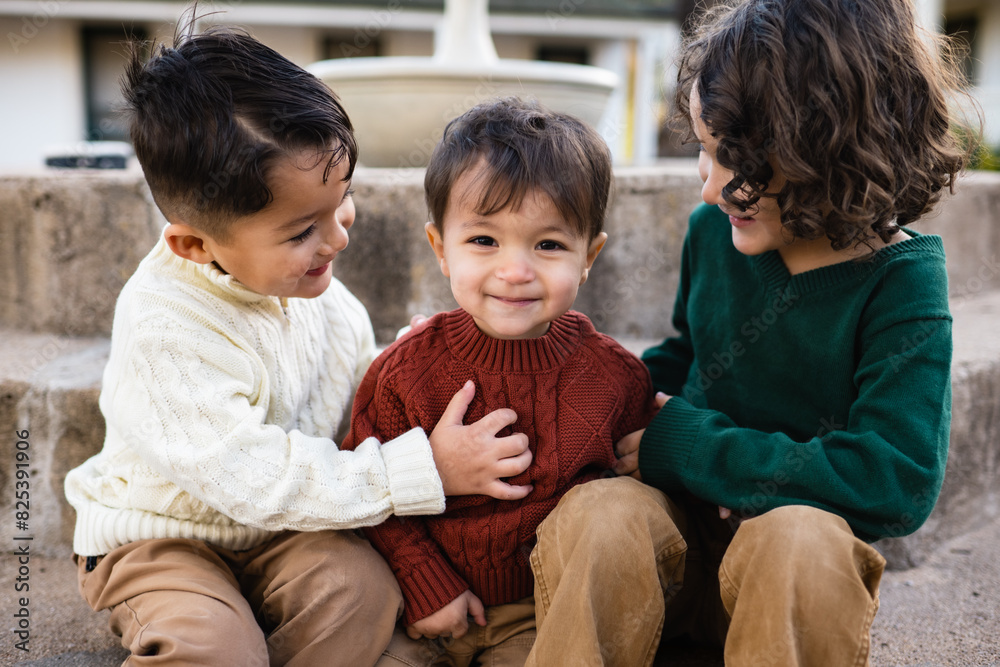 Naklejka premium Three young dark haired brothers sit on the steps of a fountain in front of a California adobe in the fall 