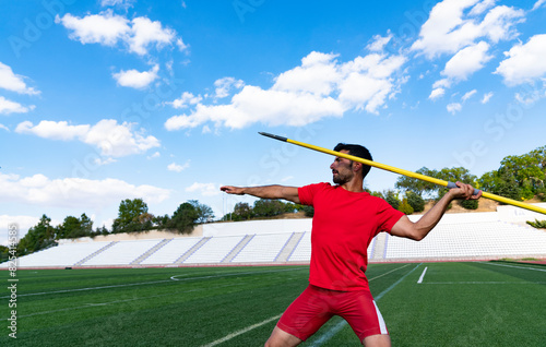 An athletic man throws the javelin in the stadium.