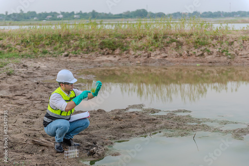 Environmental engineer Sit down next to a well while holding the plastic glass that fill with the water sample and check water quality and contaminants in the water source.