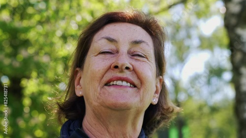 Elderly woman looking up with a smile in a park, surrounded by vibrant greenery. The sunlight illuminates her face, highlighting her joyful expression photo