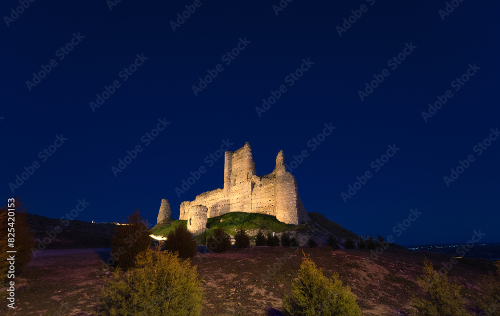 Obraz premium Castle de Santiago or Torre de los Piquillos illuminated at night under a starry sky.