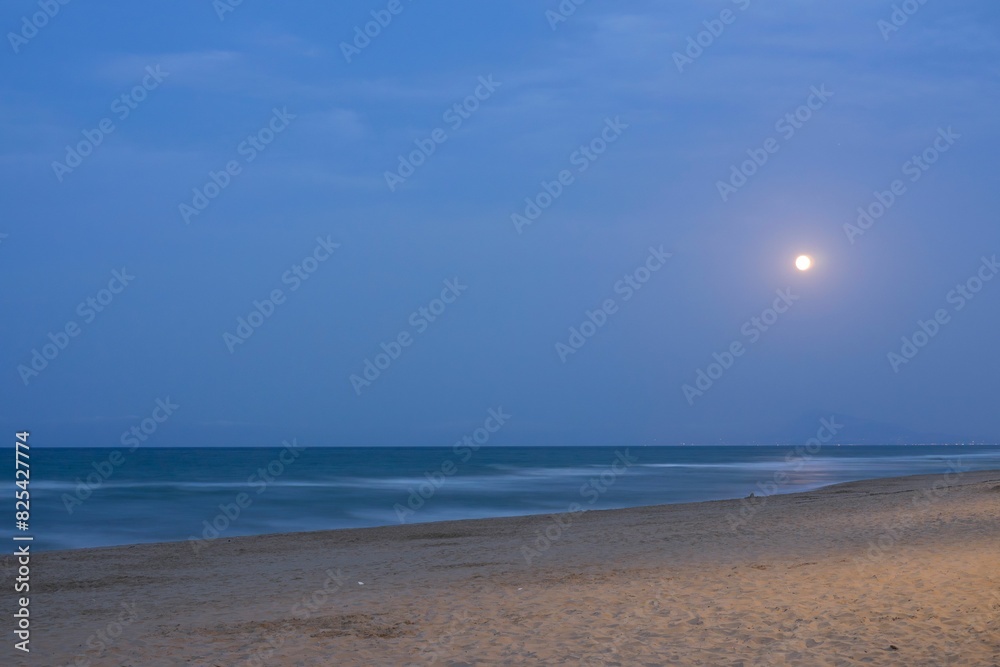 Close-up of Gandia beach with moonrise in the background of the photo.
