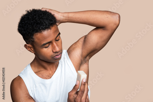 Young adult male carefully applying stick deodorant on his underarm photo
