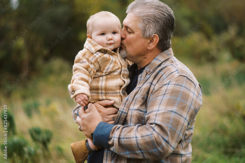 smiling grandpa holding his infant grandson in arms outdoors smiling grandpa holding his infant grandson in arms outdoors