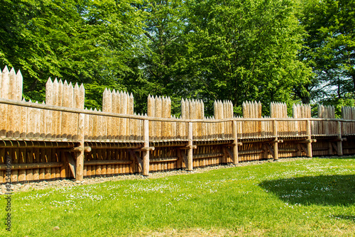 A wooden palisade from the inside of the settlement. Settlement on a sunny day. Trees and green grass. Wooden protection, stakes, fence, protection from barbarians.