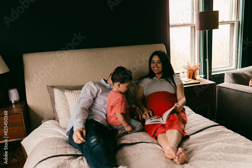 parents (incl pregnant mom)  reading to toddler on bed photo