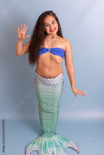 Beautiful smiling girl in a mermaid costume, friendly, standing on a blue background