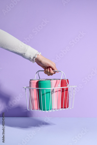 Wire shopping basket full of cans of soft drink in hand