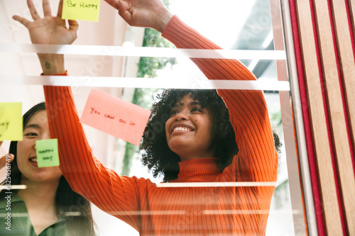 Casual businesswomen smiles while placing sticky notes on glass photo