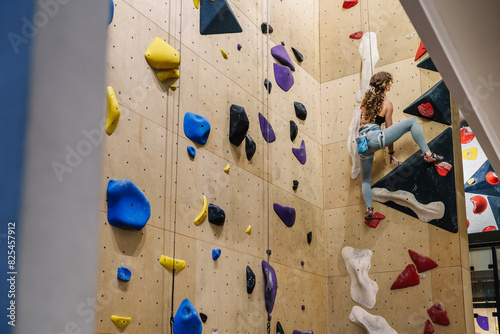 Young skilled climber training top roping at indoor climbing wall photo