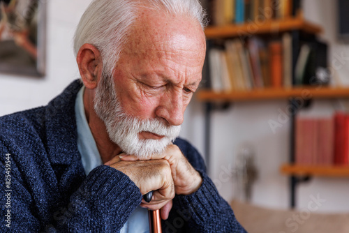 Sad senior man leaning on cane at home photo