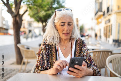 white-haired woman sitting in a cafe looking at her mobile phone