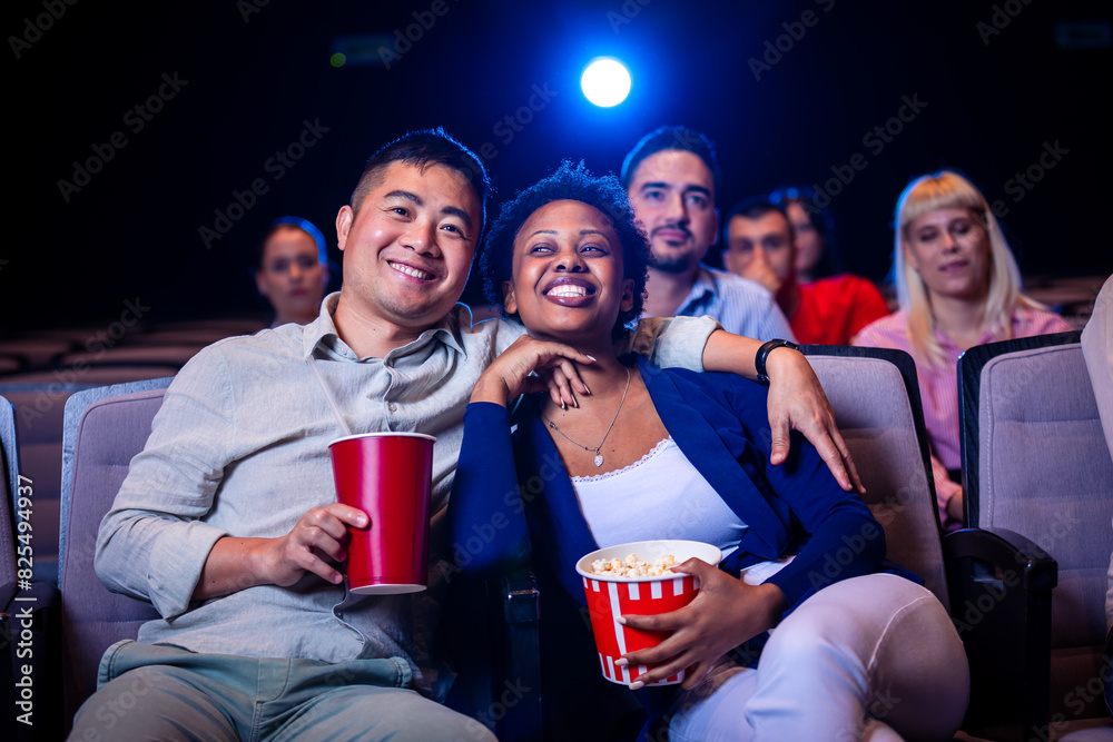 Multiracial Asian and African American couple watching a movie at cinema and eating popcorn.