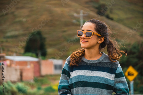 A young woman hipster traveler smiles looking towards the horizon, in the background a mountain in the middle of the road.