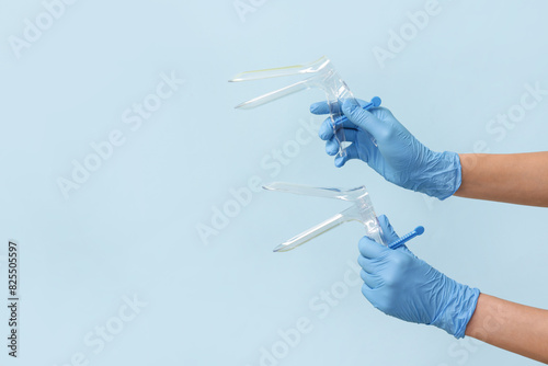Doctor hands in medical gloves with gynecological speculums on blue background photo