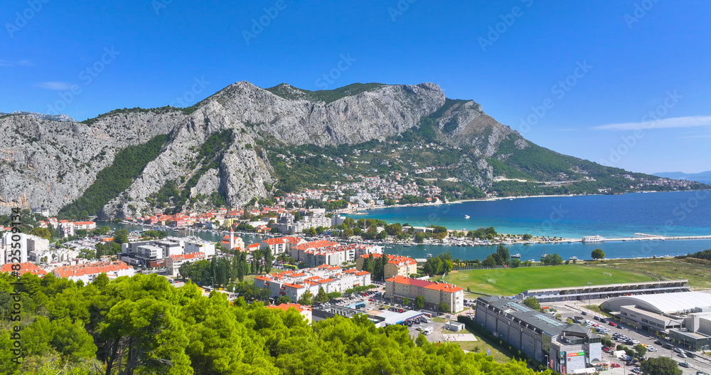 AERIAL: Scenic view of a mountain range towers above the coastal town of Omis.