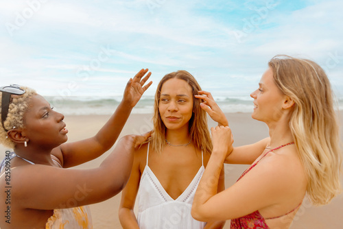 multiracial group of female friends spending the day at the beach. Two friends comb and groom another friend.