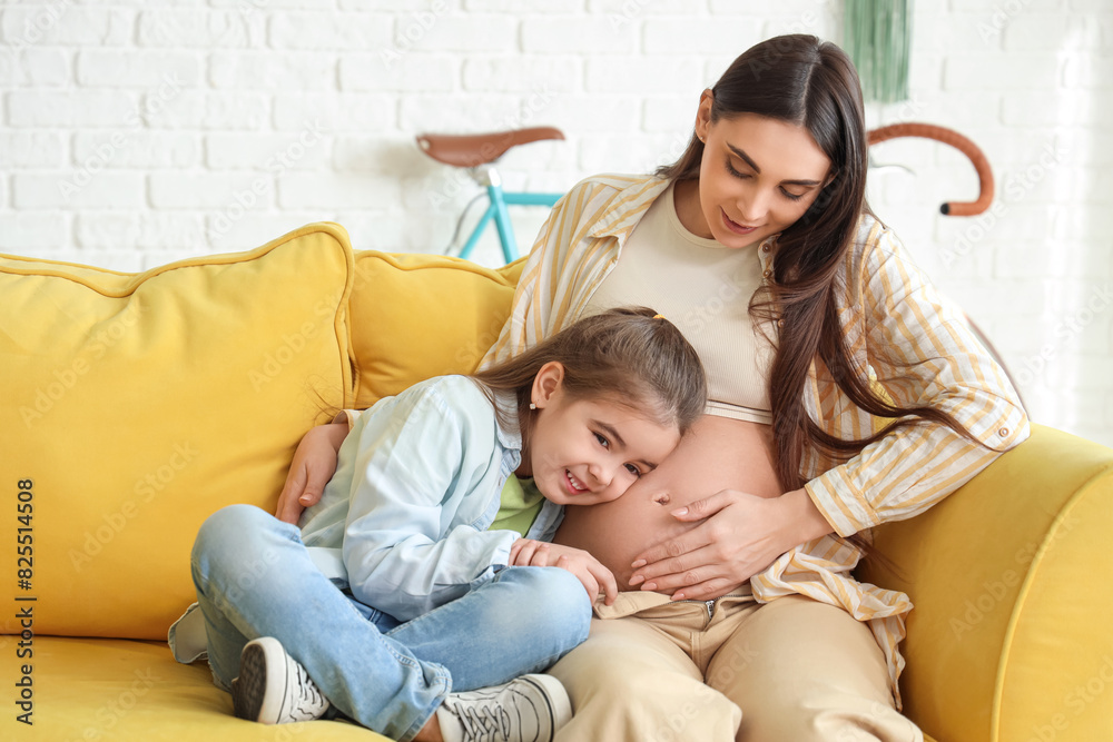 Cute little girl with her pregnant mother sitting on sofa at home Cute little girl with her pregnant mother sitting on sofa at home