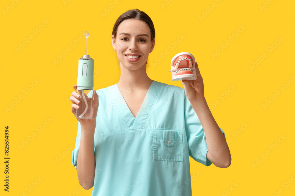 Female dentist with oral irrigator and jaw model on yellow background Female dentist with oral irrigator and jaw model on yellow background