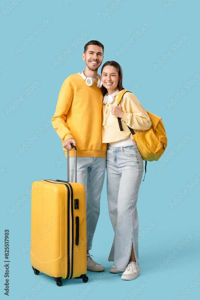 Beautiful young happy couple of tourists with headphones and suitcase on blue background Beautiful young happy couple of tourists with headphones and suitcase on blue background