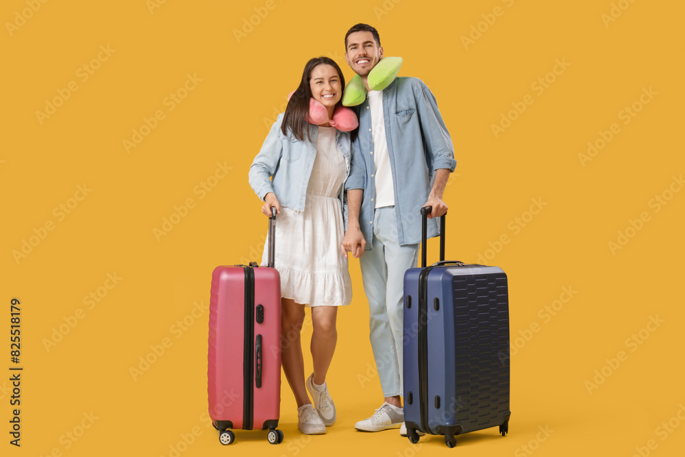 Beautiful young happy couple of tourists with suitcases and travel pillows on yellow background Beautiful young happy couple of tourists with suitcases and travel pillows on yellow background