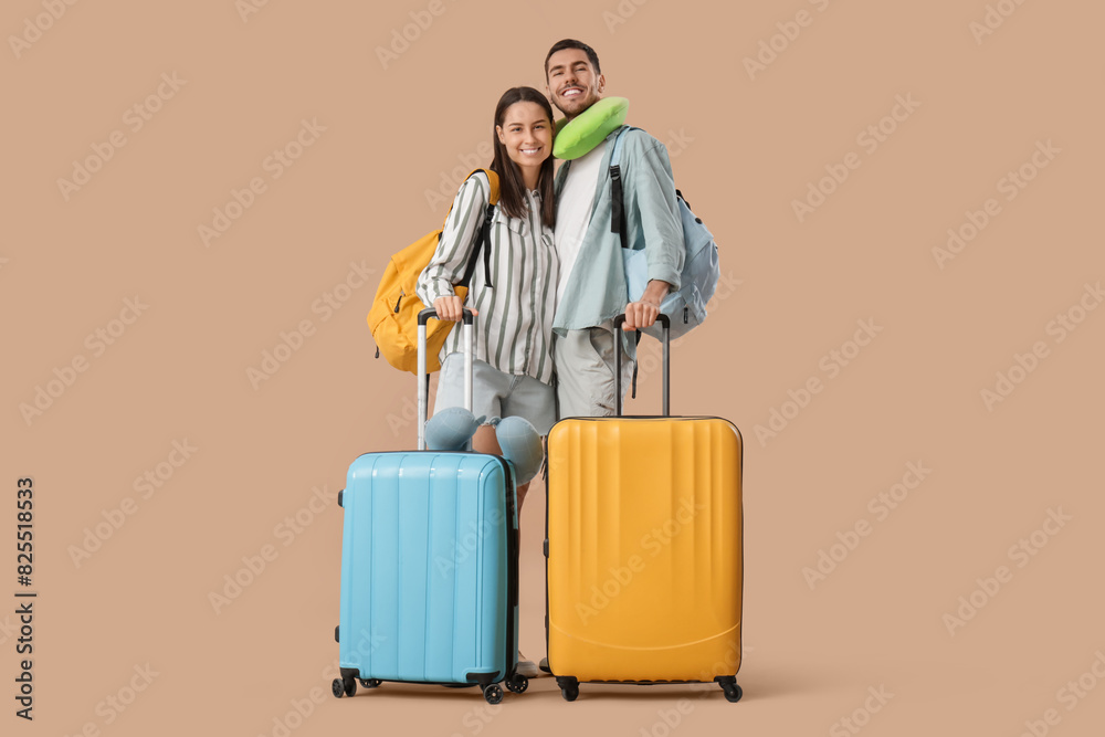 Beautiful young happy couple of tourists with suitcases, backpacks and travel pillows on brown background Beautiful young happy couple of tourists with suitcases, backpacks and travel pillows on brown background