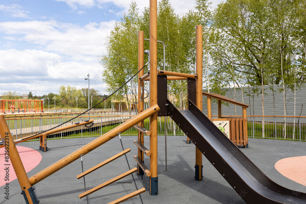 An outdoor playground featuring a wooden climbing frame with a slide, rope ladder, and swing set, surrounded by birch trees and a safety surface for children's play An outdoor playground featuring a wooden climbing frame with a slide, rope ladder, and swing set, surrounded by birch trees and a safety surface for children's play