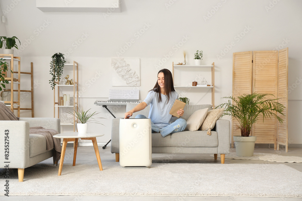 Young woman turning on humidifier in living room Young woman turning on humidifier in living room