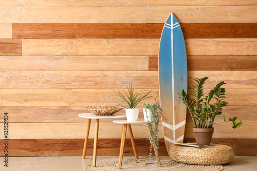 Houseplant, coffee table and surf board near wooden wall in stylish room