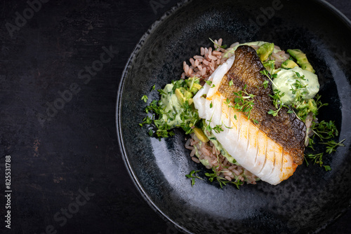 Fried skrei cod fish filet with avocado cream and boiled rice served as top view on Nordic design plate with copy space left