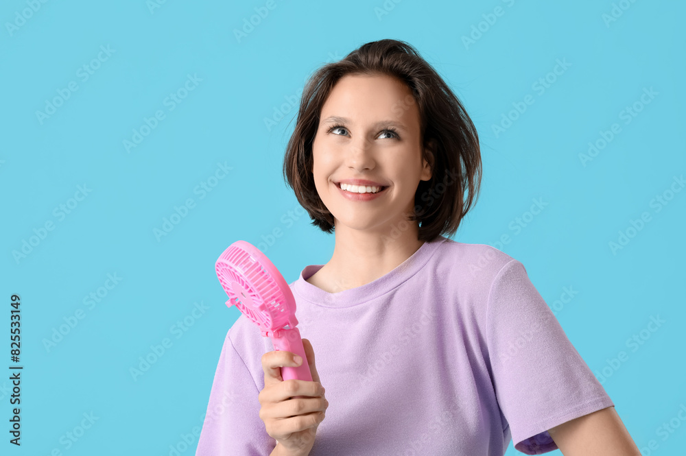 Young woman with pink portable electric fan on blue background Young woman with pink portable electric fan on blue background