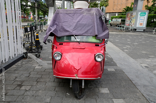 BANGKOK, THAILAND - MAY 22, 2024 : Red car Three wheeled vehicle parked on the road at the city street in Thailand.