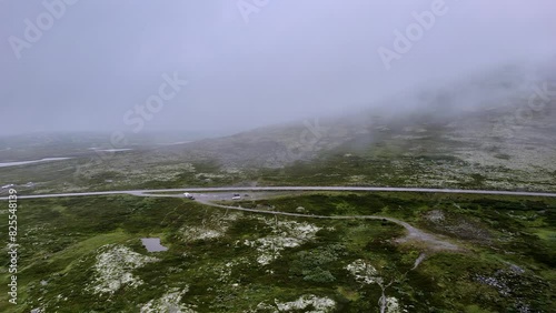 Flying over the green tundra and above a parking lot in Rondane National Park, near Venabygd, Norway, showcasing the misty nature landscape and disappearing into the cloudy mountains photo